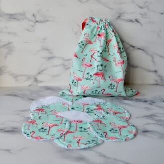 Set of reusable cotton pads with a matching storage bag. Fabric is light green with pink flamingos. The bag has a dusky pink ribbon drawstring closure