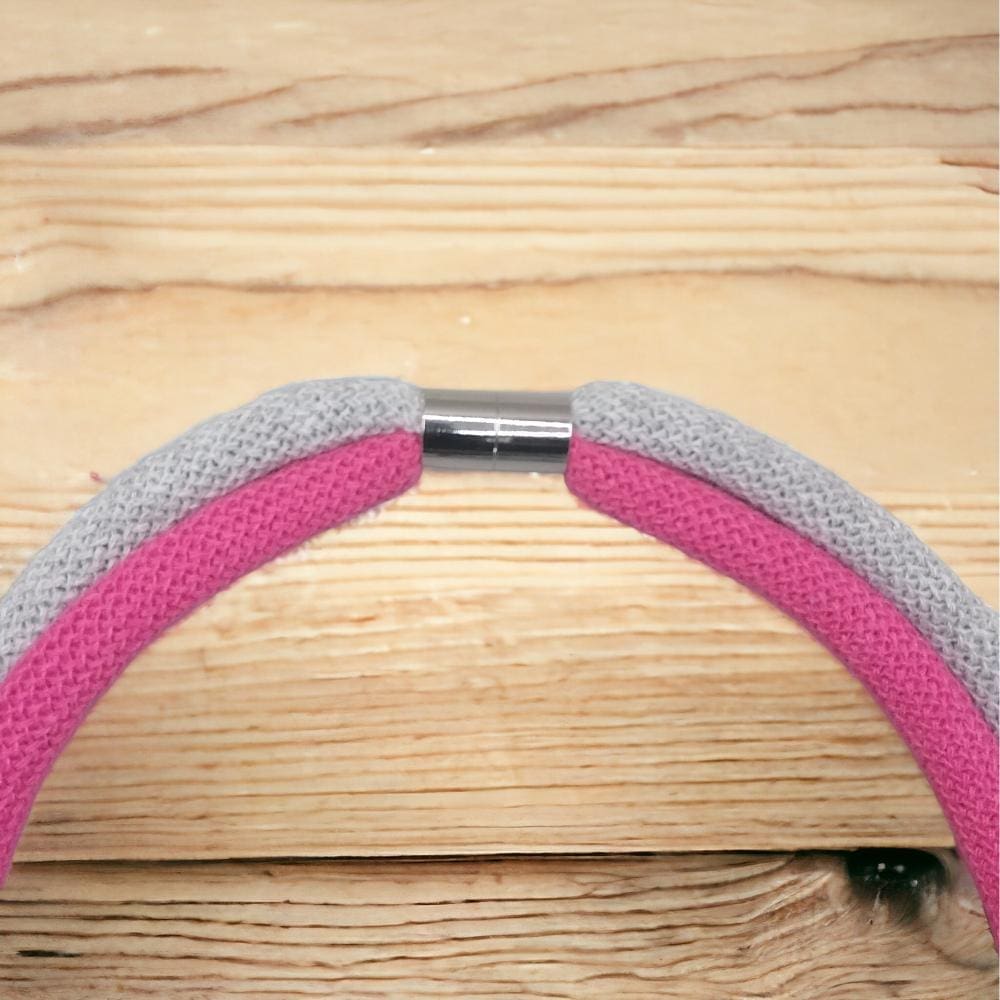 Close up of magnetic clasp feature on chunky pink and grey modern knotted macrame necklace, shown against a light wooden background.
