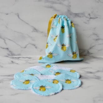 Set of reusable cotton pads with matching drawstring storage bag. Fabric is light blue with yellow bumble bees. The bag has a gold ribbon drawstring