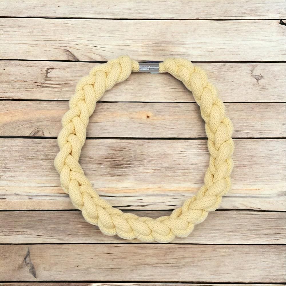 Flatlay view of chunky yellow knotted rope necklace against a light wooden background