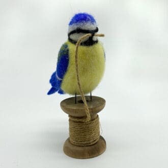 Needle felted blue tit sitting on a cotton reel with thin twin in its beak