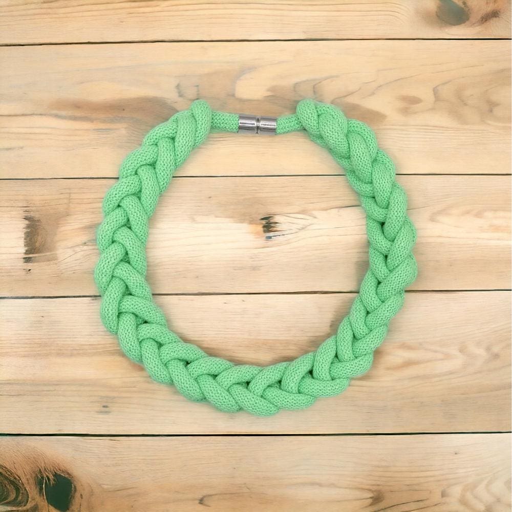 Flatlay overhead view of chunky neon green knotted rope statement necklace displayed against a light wood background