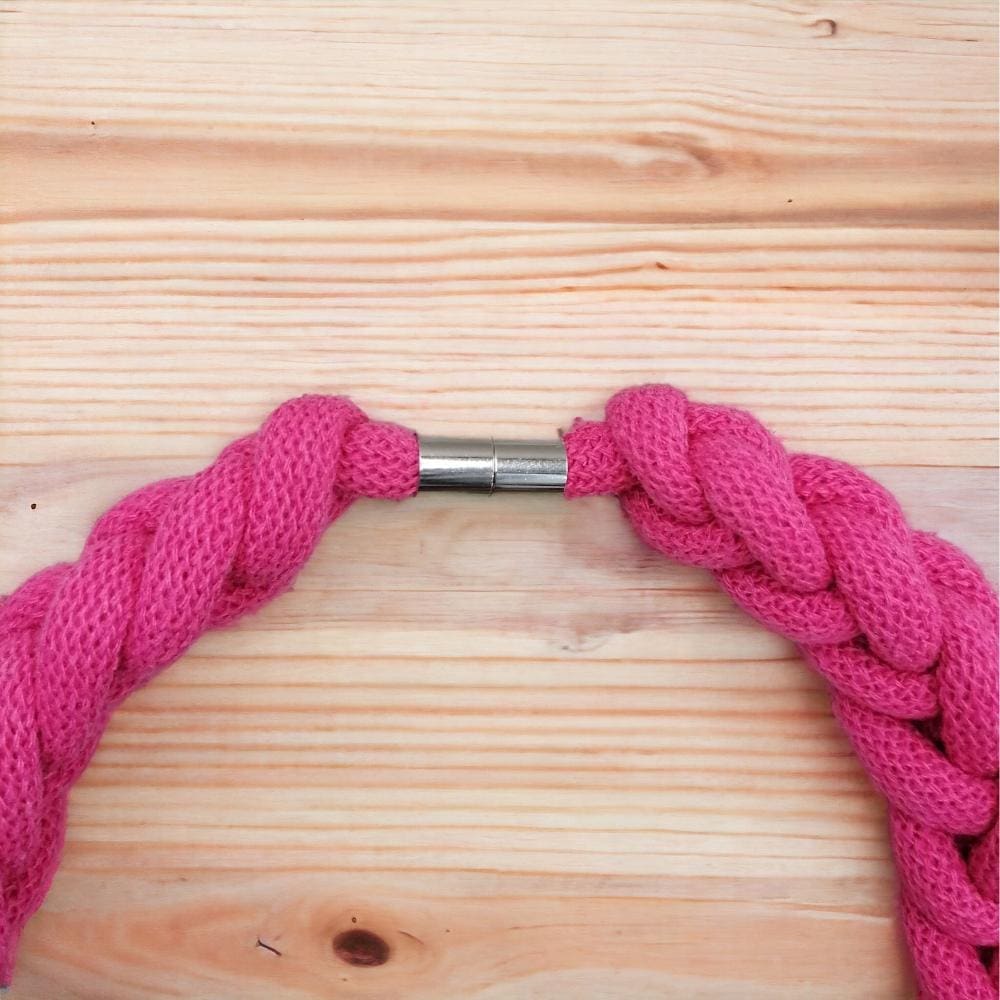 Close up of magnetic clasp detail on pink statement chunky knotted necklace, shown agains a light wood background