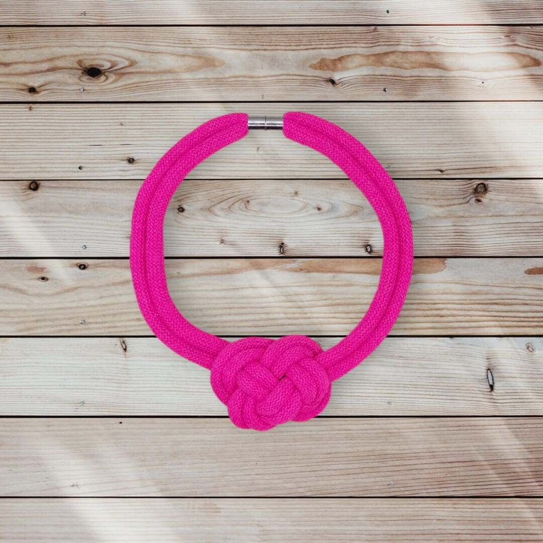 Flatlay overhead view of chunky pink statement knotted rope necklace, shown against a light wood background