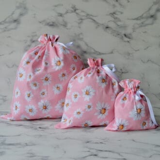 Three light pink fabric gift bags with large white daisies. From right to left - Large, medium and small bags