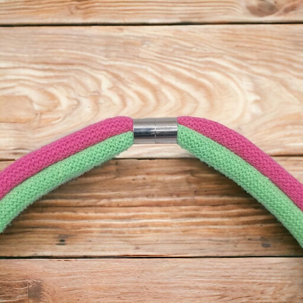 Close up of magnetic clasp feature on chunky modern pink and green statement necklace, shown against a light wooden background.