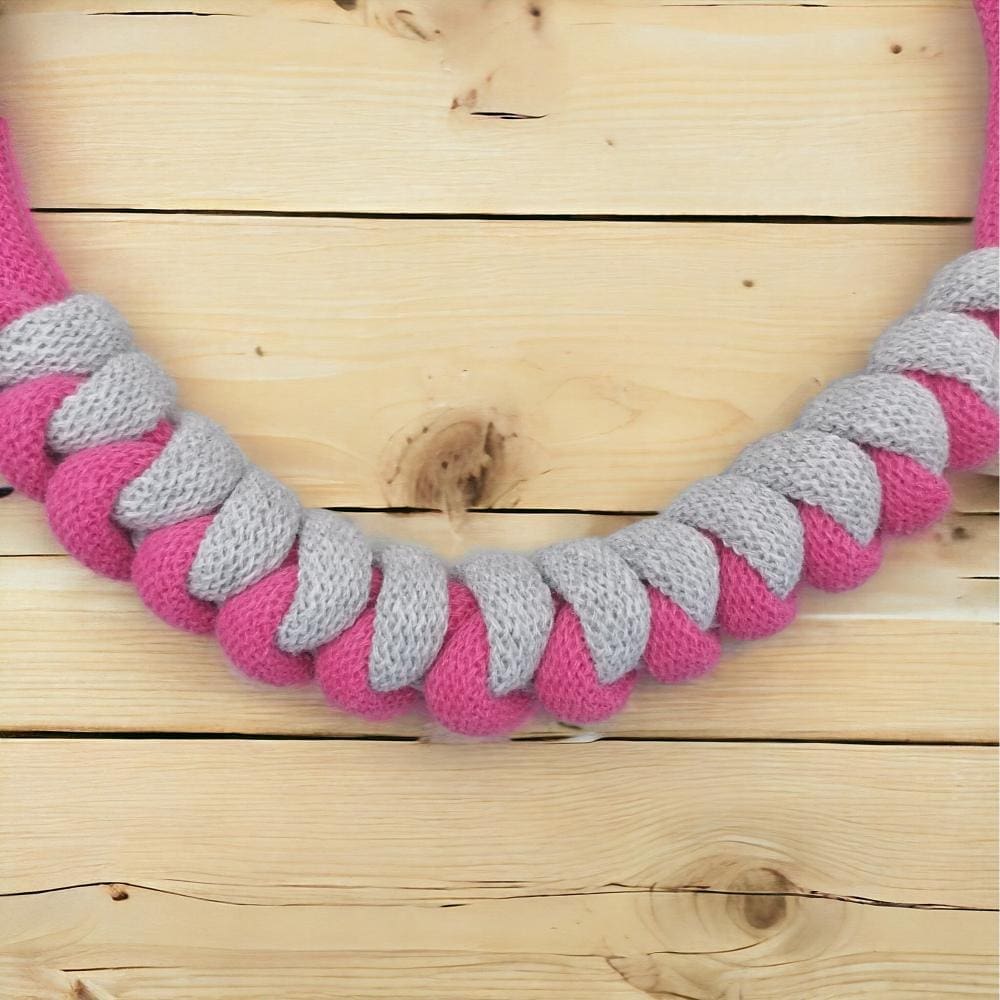 Close up of chunky pink and grey modern knotted necklace, shown against a light wooden background.