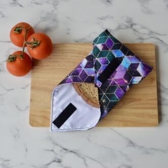 Reusable sandwich wrap on a wooden chopping board. Fabric has a purple and blue geometric square pattern.