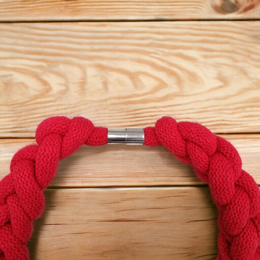 Close up of magnetic clasp detail on chunky knotted red statement necklace displayed on a light wood background