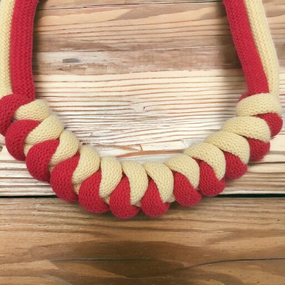 Close up of knot feature on chunky red and yellow knotted rope necklace, shown against a light wooden background.