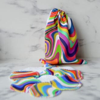 Set of reusable cotton pads with matching drawstring storage bag. Fabric is a wavy retro rainbow design.