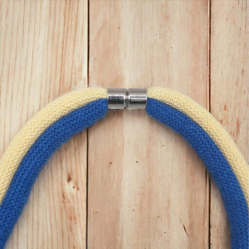 Close up of magnetic clasp feature on funky blue andyellow chunky knotted necklace made from recycled cotton cord, shown against a light wooden background.