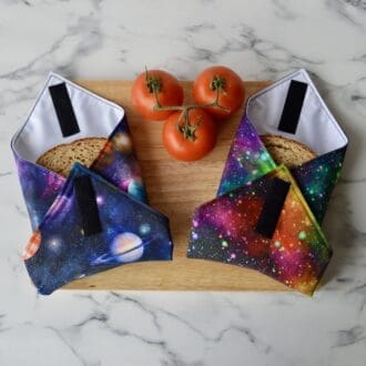 Two sandwich wraps on a wooden chopping board. Left wrap is navy with planets. Right sandwich wrap is black with starbursts in multiple colours