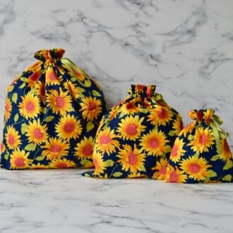 A set of three reusable fabric gift bags, each in navy with large yellow sunflowers and green ribbon drawstring closures.