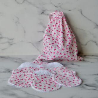 Set of reusable cotton pads with matching storage bag. Fabric is white with small pink flamingos. The bag has a light pink ribbon drawstring closure
