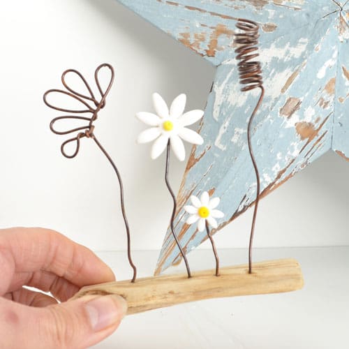 Wire and clay flowers set on a piece of driftwood, handmade ornament