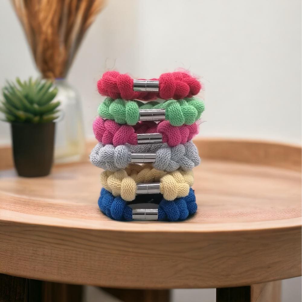 groups of colourful chunky knotted rope bracelets stacked on top of each other on a wooden countertop.