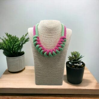 Pinnk and green knotted statement chunky necklace on a model bust shown against a light background.