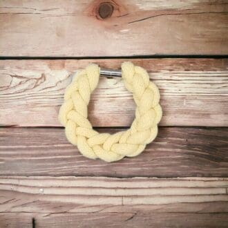 Yellow chunky knotted rope statement bracelet viewed from above against a wodden countertop background.