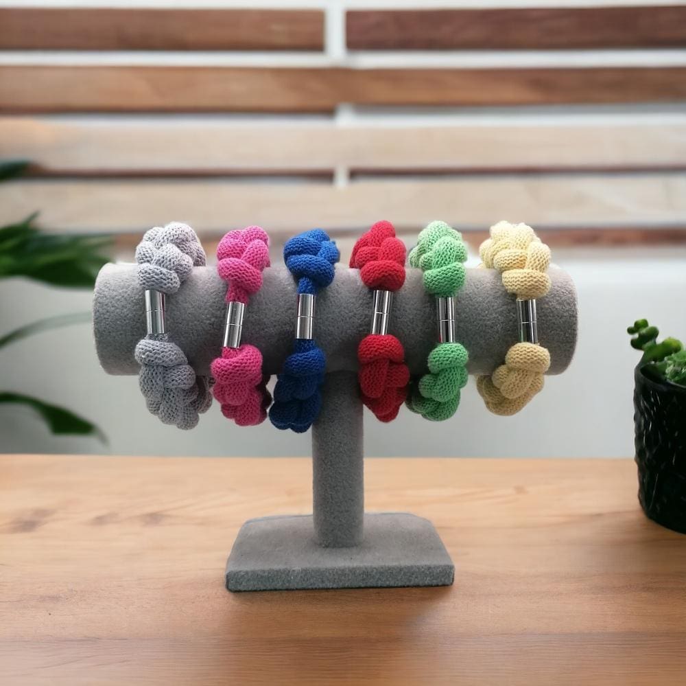 Group of colourful chunky statement knotted rope bracelets displayed on a stand atop a wooden countertop.