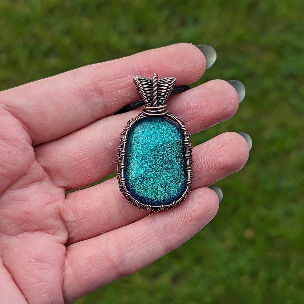 Hand holding a copper wire wrapped pendant with green dichroic glass
