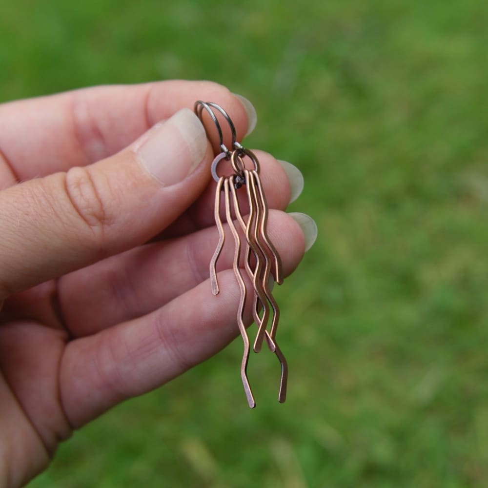 Hand holding a pair of long copper zigzag earrings