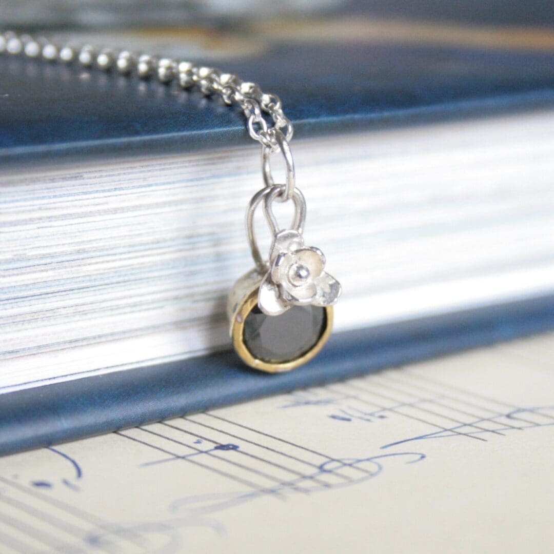 A dainty sterling silver charm necklace with a black cubic zirconia in a collet setting and a little sliver flower.