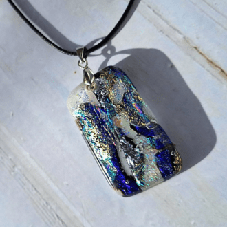 A close-up photo of a beautiful handmade dichroic glass pendant. The dichroic glass shimmers with vibrant colors that change depending on the angle of light. The pendant has a silver-plated pinch bail and hangs from a black corded necklace (approximately 18 inches long).