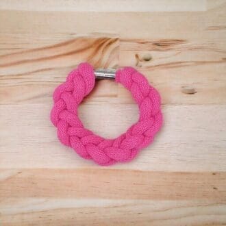 Pink chunky knotted rope statement bracelet shown on a light wood countertop