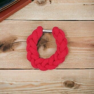 Chunky red knotted rope statement bracelet shown from above against a light wooden background.