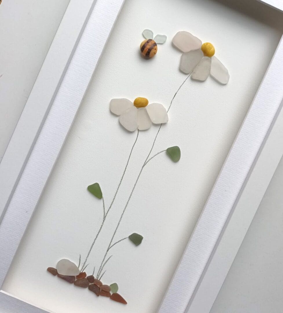 three tall daisies with petals made from nuggets of Cornish sea glass set inside a long frame