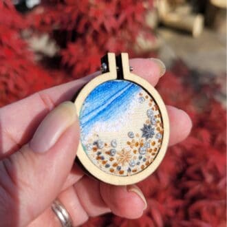 Mini embroidery hoop brooch 4cm. Embroidered shoreline with pebbles and seashells.