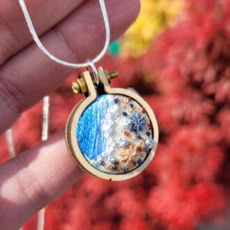 Hand embroidered shoreline pendant set in a 2.5 cm mini embroidery hoop frame.