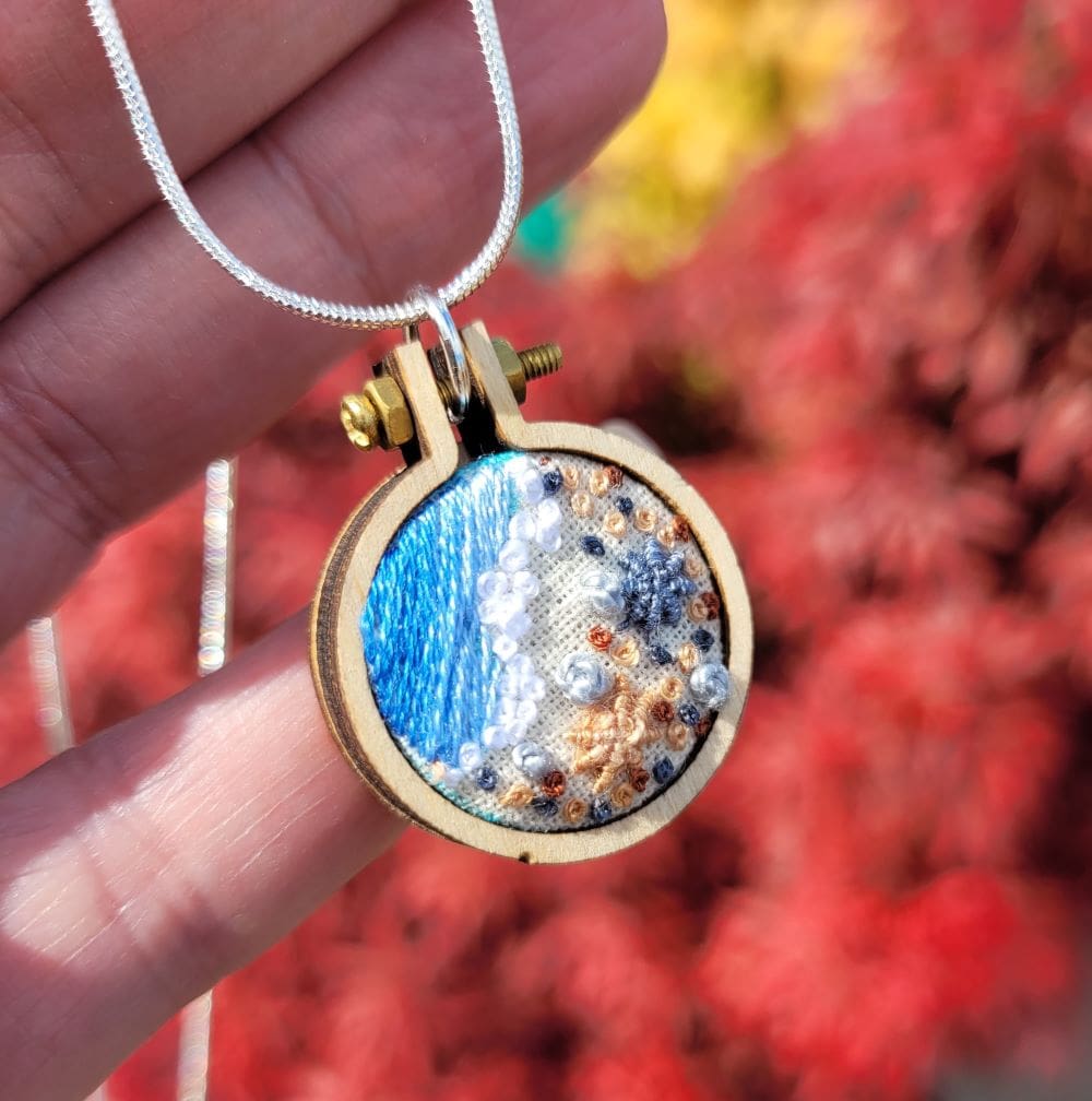 Hand embroidered shoreline pendant set in a 2.5 cm mini embroidery hoop frame.