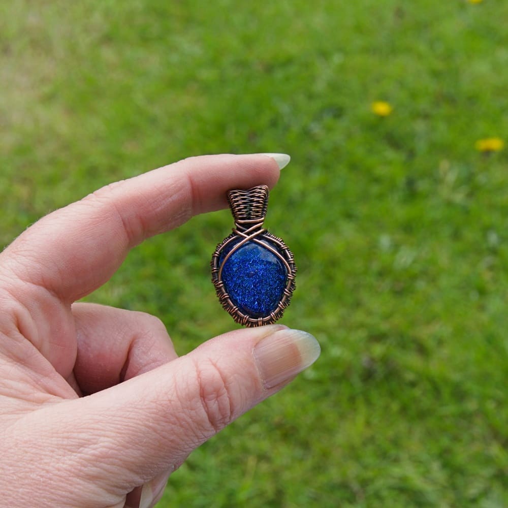 Hand holding a small copper pendant with blue dichroic glass nugget