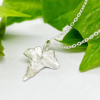 Silver ivy leaf necklace next to a bright green ivy leaf