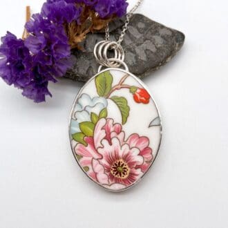 pendant made from an oval shaped piece of broken pottery with flower design set in sterling silver on a silver chain