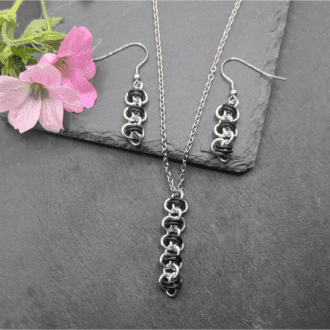 A earring and necklace set made from a section of barrel weave chainmaille in silver and matt black rings.