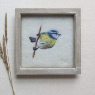 A blue-tit bird picture needle felted by hand with wool onto a natural cream felt background and in a pale wood box frame.