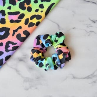 A brightly coloured scrunchie with vibrant stripes of pink, yellow, lilac, orange, green and blue with black leopard markings