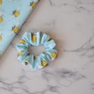 A light blue scrunchie featuring yellow and black bumble bees.
