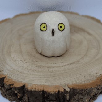 Ceramic snowy owl with yellow eyes on a wooden round with white background