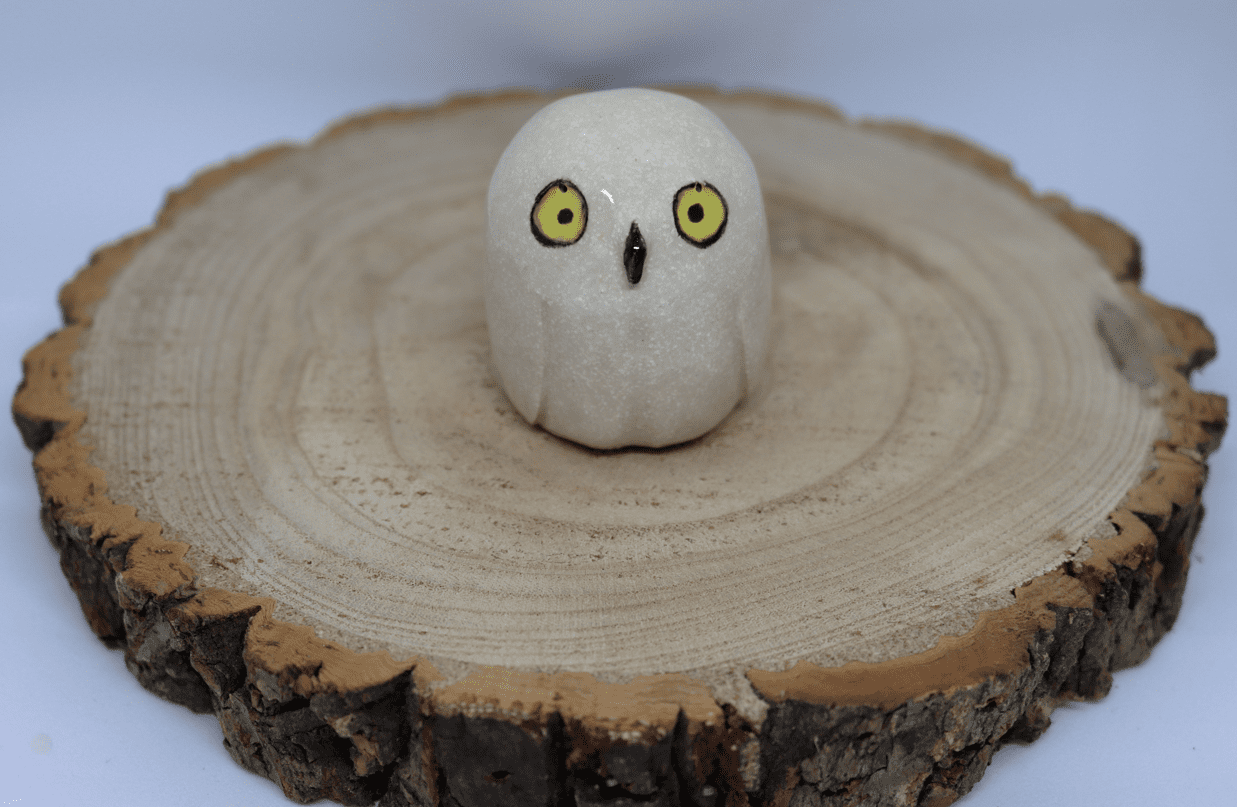 Ceramic snowy owl with yellow eyes on a wooden round with white background