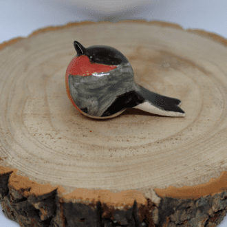Ceramic bullfinch on a wooden round with white background