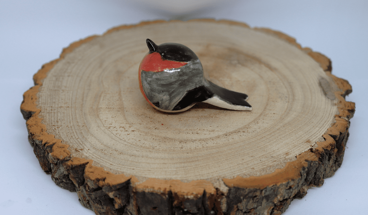 Ceramic bullfinch on a wooden round with white background