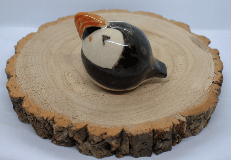 Ceramic puffin facing left on a wooden round on a white background