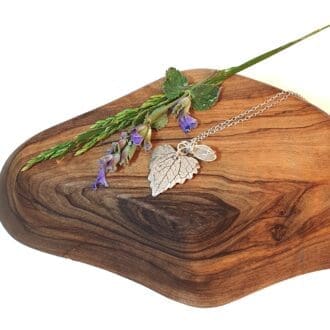 A silver leaf & seaglass necklace on a wooden block