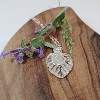 Silver hazel leaf & white silver wire wrapped pendant on olive wood next to cat mint sprig