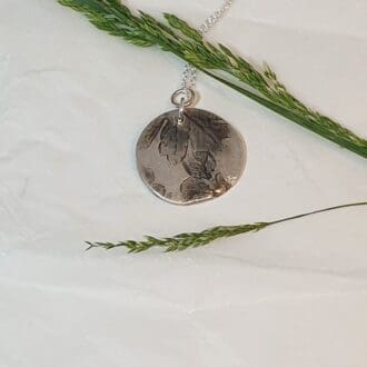 Solid silver Hawthorn flower & leaf imprint pendant displayed on a plain white background with some grass