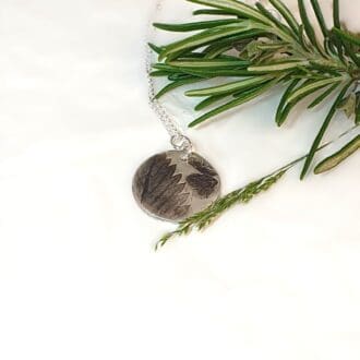 strawberry leaf imprint silver pendant on white background with a spring of rosemary